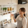 賃貸キッチンに設置されたおしゃれな白い吊り棚を見上げて微笑む日本人女性。デッドスペースを有効活用している様子。